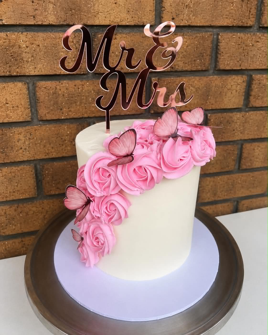 Single tier white buttercream wedding cake with cascading pink rose buttercream, pink butterfly decorations and a rose gold Mr & Mrs acrylic topper